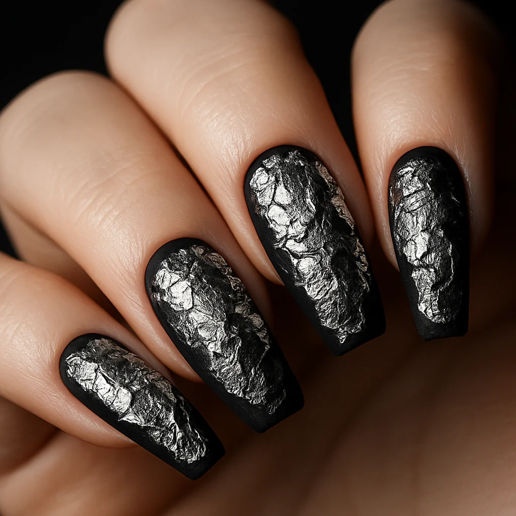 Black matte nails with crinkled silver foil patches in organic shapes on pale fair skin raking studio light — textured black nail 2026