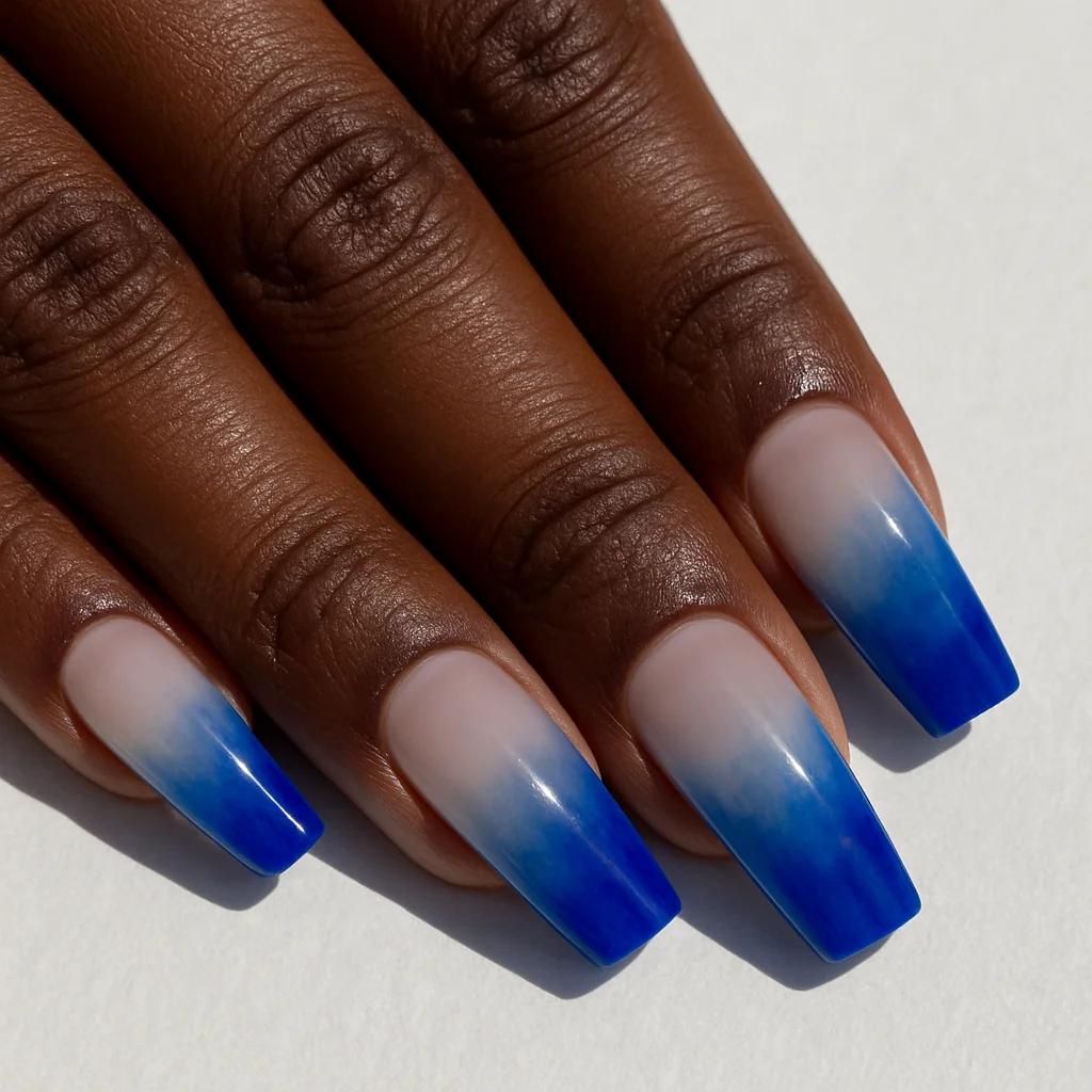 Cobalt blue ombre French gradient tip on clear base on dark brown skin on white tiles overhead — ombre french tip 2026