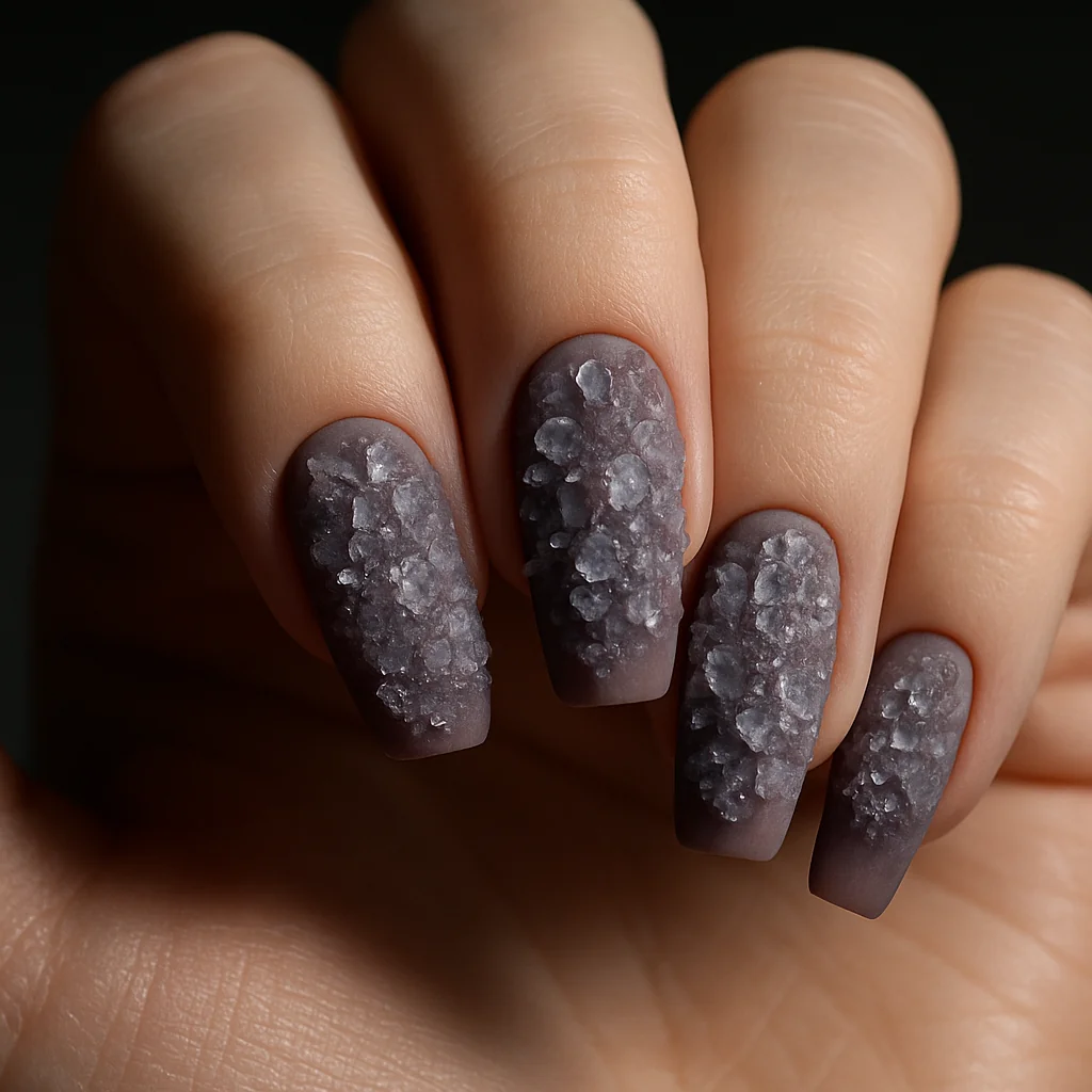 Druzy geode crystal cluster texture on dusty mauve matte base on pale cool skin raking light — organic gem nail 2026
