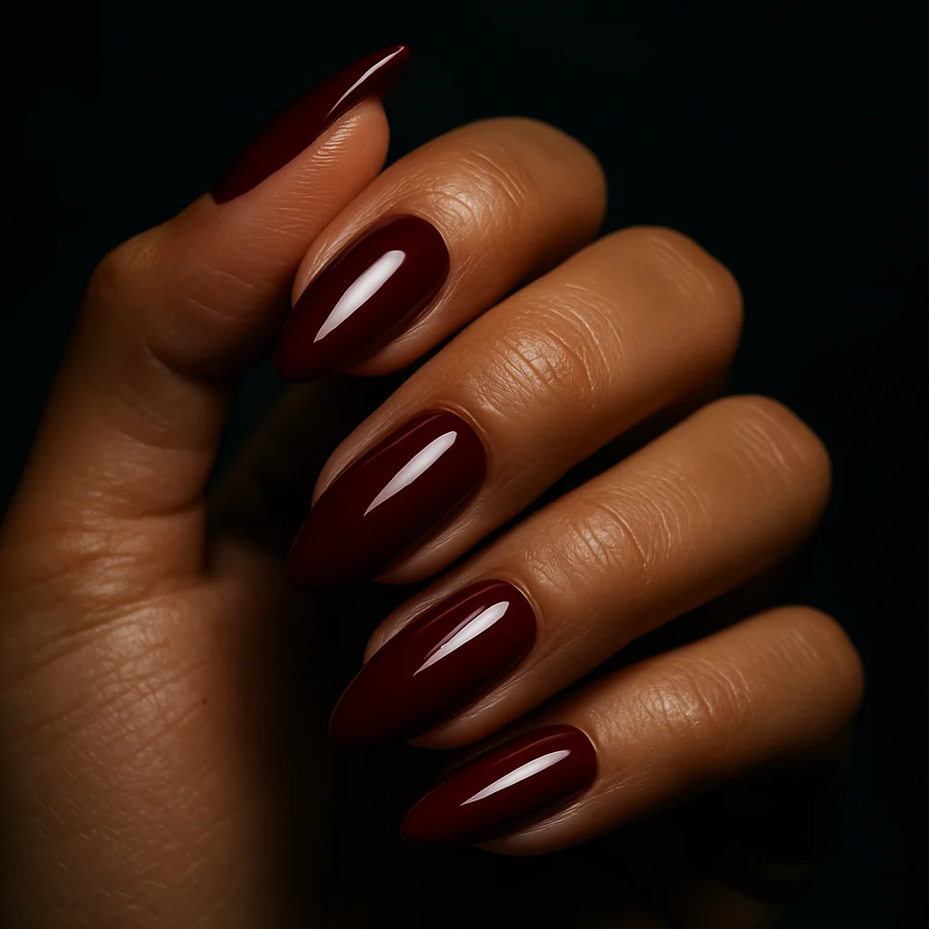 Short almond nails in deep oxblood red glossy gel on warm tan skin from below — dramatic nail design 2026